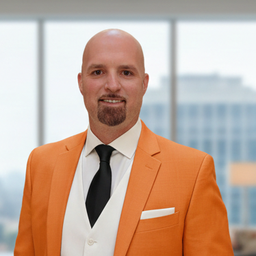 Ein Mann in einem orangefarbenen Anzug mit schwarzer Krawatte lächelt in moderner Büroumgebung.